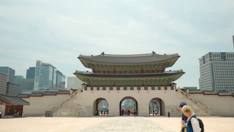 Gwanghwamun-Gate-and-two-tourists-walk-along-the-square-of-Gyeongbokgung-Palace-on-a-summer-day---copy-space