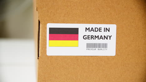 Hands-applying-MADE-IN-GERMANY-flag-label-on-a-shipping-cardboard-box-with-products