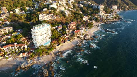 blue-ocean-waves-crashing-on-the-coastline-beach-of-Playa-Amapas-in-Puerto-Vallarta-Mexico-at-sunset,-aerial