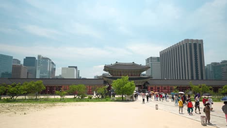 Travel-tour-senior-group-of-People-passed-Heungnyemun-Gate-and-crossed-Yeongjegyo-bridge-at-Gyeongbokgung-Palace-with-a-view-of-the-Government-Seoul-Building-and-skyscrapers-against-blue-sky