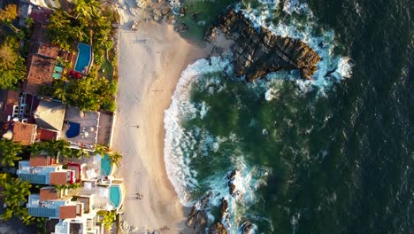 top-down-view-of-beautiful-white-sand-rocky-beach-at-Playa-Amapas-in-Puerto-Vallarta-Mexico-at-sunset,-aerial