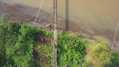Birds-Eye-View-of-a-motorcycle-that-crosses-a-suspension-bridge-over-a-large-muddy-river-in-Central-Java-Indonesia