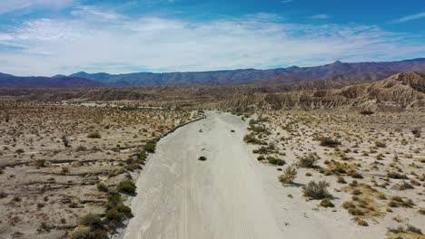 Flying-above-a-dirt-road-through-a-colorful-but-barren-desert-landscape