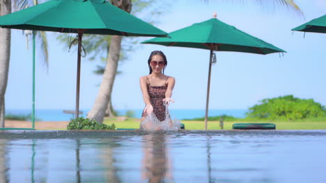 Sexy-Exotische-Frau-Im-Schwimmbad-Des-Luxuriösen-Tropischen-Resorts,-Die-Spaß-Hat,-Wasser-Sprüht,-Zeitlupe