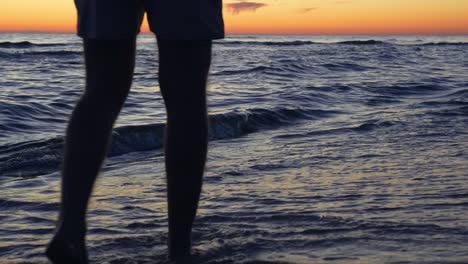 Rear-view-of-young-man's-legs-walking-on-seashore-at-sunset,-slow-motion