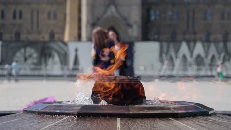 Centennial-Flame-burning-on-a-hot-and-sunny-summer-day-on-Parliament-Hill,-Ottawa,-Canada-with-tourists-taking-photos-of-the-Parliament-building-in-the-background---4K-slow-motion