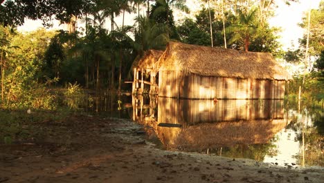 two-huts-with-palm-tree-roofs-that-stand-in-the-water-of-the-Amazon-River-and-reflect-in-the-water