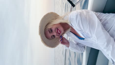 Young-beautiful-caucasian-woman-in-a-white-shirt-with-a-fedora-hat-sitting-on-the-boat