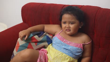Cute-asian-little-girl-sulking-while-siiting-on-the-sofa-at-home