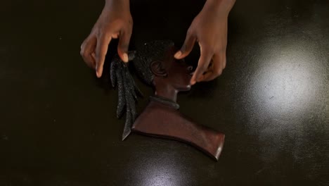 Top-down-shot-of-an-African-American-man's-hands-placing-a-female-wooden-African-mask-on-a-brown-table