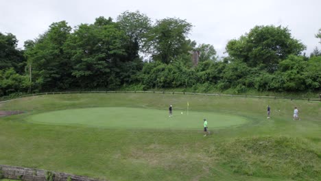 golfers-walking-to-hole-on-green,-aerial-drone-panning
