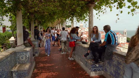 Tourists-Sitting-on-Edge-of-Miradouro-de-Santa-Luiza-accompanied-by-artists-showing-their-illustrations-of-Lisbon,-and-by-musicians-providing-a-soundtrack