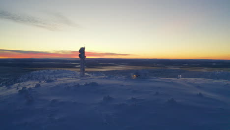 Aerial-view-rising-above-sunrise-remote-Nordic-Lapland-cabin-and-communications-tower-in-polar-snow-covered-wilderness