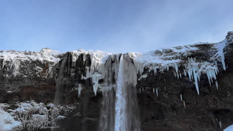 Tilt-down-shot-of-spectacular-icy-Seljalandsfoss-Waterfall-in-winter-during-sunlight