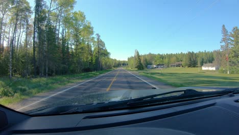 POV-while-driving-on-a-narrow-county-road-past-past-a-few-rural-homes-in-forested-area-of-northern-Minnesota-in-early-spring