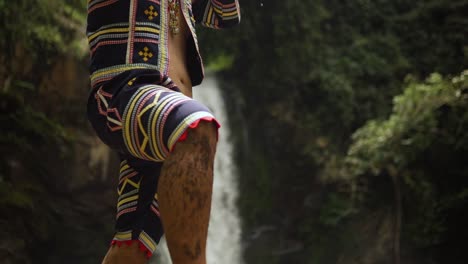 Indigenous-person-playing-Kubing-tribal-instrument,-behind-is-a-waterfall-while-standing