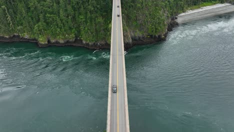 Top-down-drone-shot-tracking-a-car-across-a-bridge-over-the-ocean