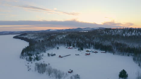 Aerial-view-quiet-secluded-wild-rural-snow-covered-cabins-surrounded-by-Scandinavian-woodland-wilderness