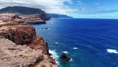 Windturbinen-Am-Rand-Der-Klippe-In-Der-Nähe-Von-Miradouro-Da-Ponta-Do-Rosto-Mit-Paar-Touristen-In-Ost-Madeira,-Portugal