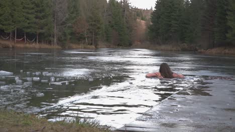 Extreme-adventure-as-woman-swims-in-hole-cut-into-frozen-surface-of-lake-then-rests-on-ice-ledge-and-smiles