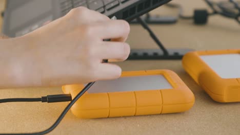 A-hand-connects-an-orange-Lacie-hard-drive-to-a-pc