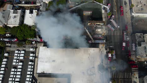 Firefighters-extiguishing-a-burning-and-smoking-structure-in-a-city---Aerial-view