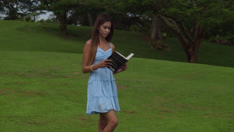 A-young-girl-opens-a-book-while-walking-on-a-golf-course-on-the-tropical-island-of-Trinidad