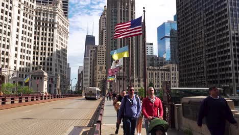 Menschen,-Die-über-Die-Stadtbrücke-Mit-Amerikanischen-Und-Ukrainischen-Flaggen-Gehen,-Skyline-Der-Innenstadt