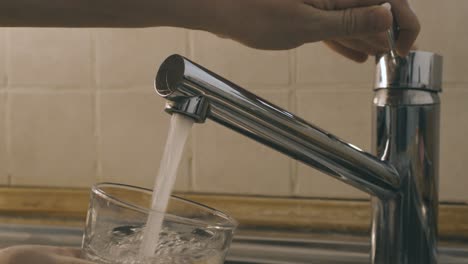Two-hands-turn-on-the-water-from-the-kitchen-sink-faucet-and-fill-a-glass-with-water