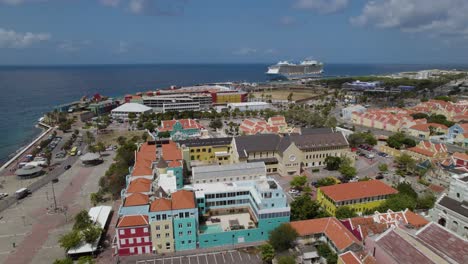 Aerial-establishing-shot-of-the-historical-center-of-Willemstad,-Curaçao-with-a-giant-cruise-ship-in-the-background