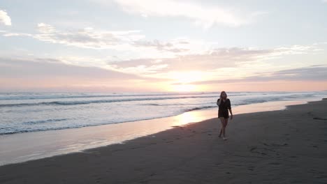 Young-woman-walking-back-from-the-warm-south-pacific-ocean-with-a-magnificent-sunset-in-the-background