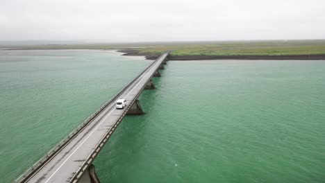 Brücke-über-Wasser-In-Island-Mit-Autofahren-Und-Drohnenvideo-Dahinter