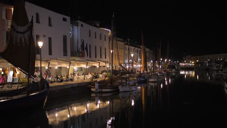 Pan-shot-of-Old-town-along-Da-Vinci-canal-waterway-in-Cesenatico,-Northern-Italy-with-the-view-of-an-outdoors-restaurant-packed-with-tourists-at-night-time