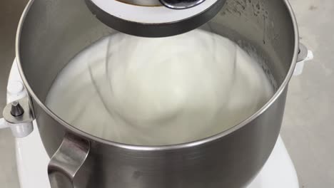 Commercial-bakery-setting-close-up-shot-of-electric-mixer-mixing-egg-white-and-sugar-until-it-is-glossy-peak-and-stiff-peak,-preparing-meringue-buttercream