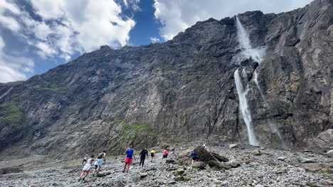 people-hiking-along-the-river,-to-reach-the-big-waterfall-of-cirque-de-Gavarnie,-famous-french-landscape-of-pyrenees-mountains