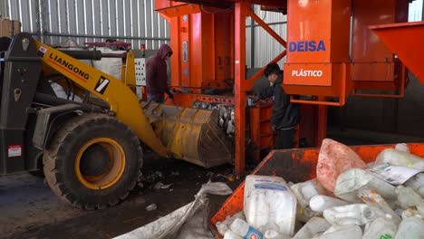 Medium-view-of-workers-loading-compacted-waste-onto-a-bulldozer-inside-a-waste-processing-plant