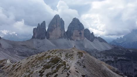 Aerial-rotation-view-of-a-man-standing-alone-on-a-mountain-peak-with-a-view-over-Tre-Cime-di-Lavaredo-after-a-successful-and-adventurous-hike-in-the-Dolomites-of-North-Italy