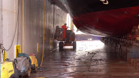 Shipyard-worker-cleaning-mussels-and-dirt-from-ships-hull-inside-floating-dry-dock---Westcon-olensvag-Norway