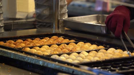 Japanese-cuisine-takoyaki-balls-close-up-shot,-professional-chef-making-the-crispy-street-food-on-hot-molded-pan-at-busy-night-market-in-Taiwan,-Asia