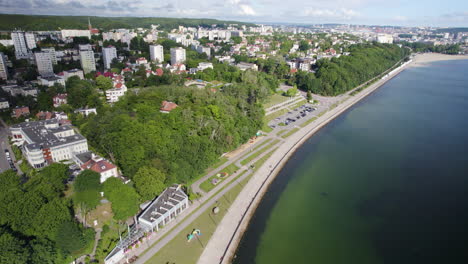 Aerial-view-showing-shoreline-of-Baltic-Sea-in-Gdynia-City-with-apartment-blocks,-forest-and-downtown-in-backdrop