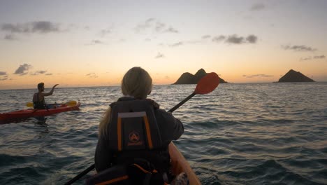 Couple-paddling-kayaks-on-sea-towards-sunset,-Hawaii,-slow-motion