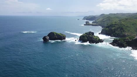 Aerial-view-of-rock-island-in-ocean,hit-by-waves-during-sunny-day---TIMANG-ISLAND,-YOGYAKARTA,-INDONESIA
