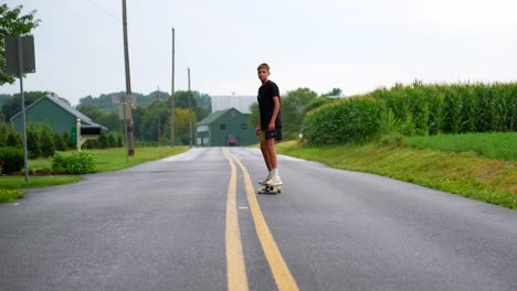 Low-shot-of-teenage-boy-riding-skateboard-in-the-middle-of-a-road