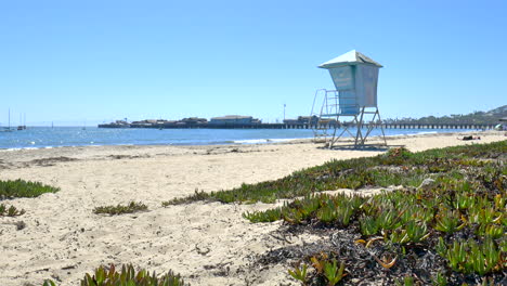 Standing-on-the-sandy-beach-watching-the-blue-waves-against-the-shore-with-an-empty-lifeguard-tower-on-a-sunny-clear-day-in-Santa-Barbara,-California