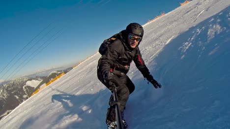 Vista-Frontal-De-Un-Snowboarder-Bajando-A-Alta-Velocidad-Con-Un-Selfie-Stick-Y-Casi-Cayendo