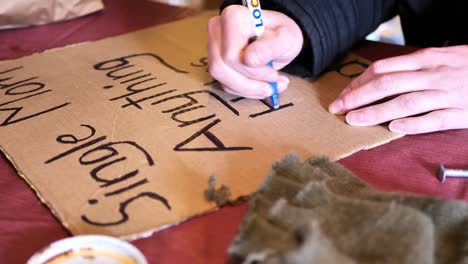 Homeless-women-tracing-over-and-making-cardboard-sign-saying,-"Single-mom,-anything-helps,-God-bless"