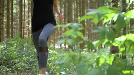 Blonde,-fit-woman-jogging-through-the-woods-runs-past-the-camera-as-it-moves-across-her-path-at-a-low-angle
