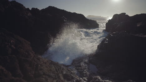 Medium-tilt-down-shot-of-splashing-ocean-wave-on-rocks-at-sunny-day-in-Ucluelet,-Vancouver-Island,-Canada