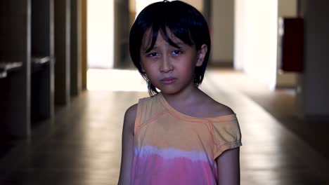 Portrait-of-a-young-Southeast-Asian-boy-alone-scared-looking-into-camera-in-an-abandoned-mall-hallway-with-light-and-shadow-in-the-background