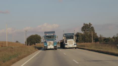 Two-Peterbilt-semi-eighteen-wheeler-trucks-driving-down-the-highway-in-evening-sun-side-by-side-in-slow-motion